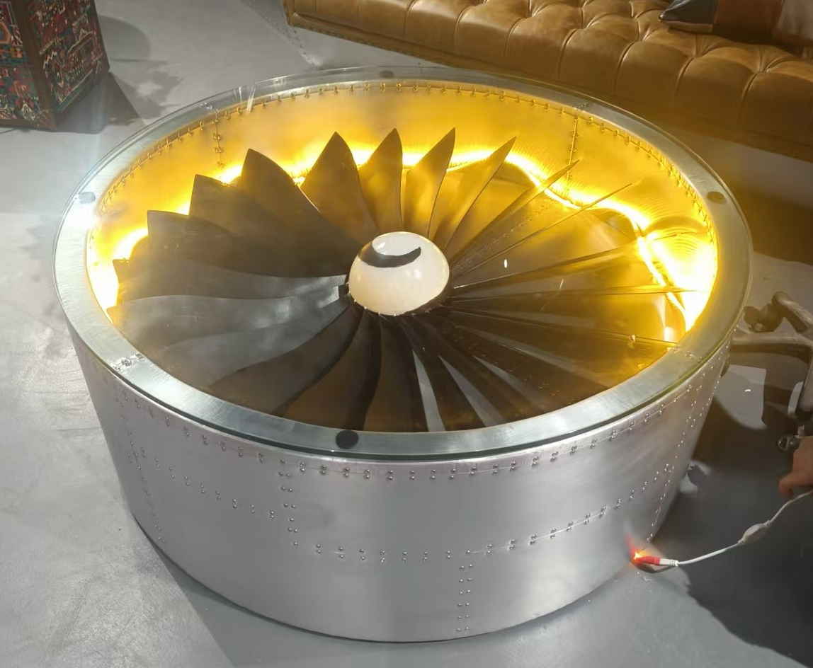 The Aviator jet turbine coffee table: a polished jet engine fan set beneath glass in a riveted aluminium nacelle, glowing amber from within